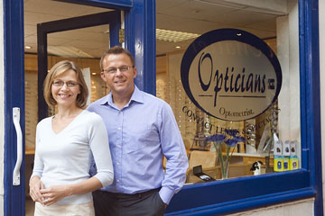 an eyeglass-wearing couple standing outside an optician shop